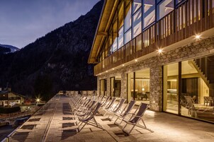 A hotel with a terrace featuring sun loungers, stone walls, and a mountain backdrop.