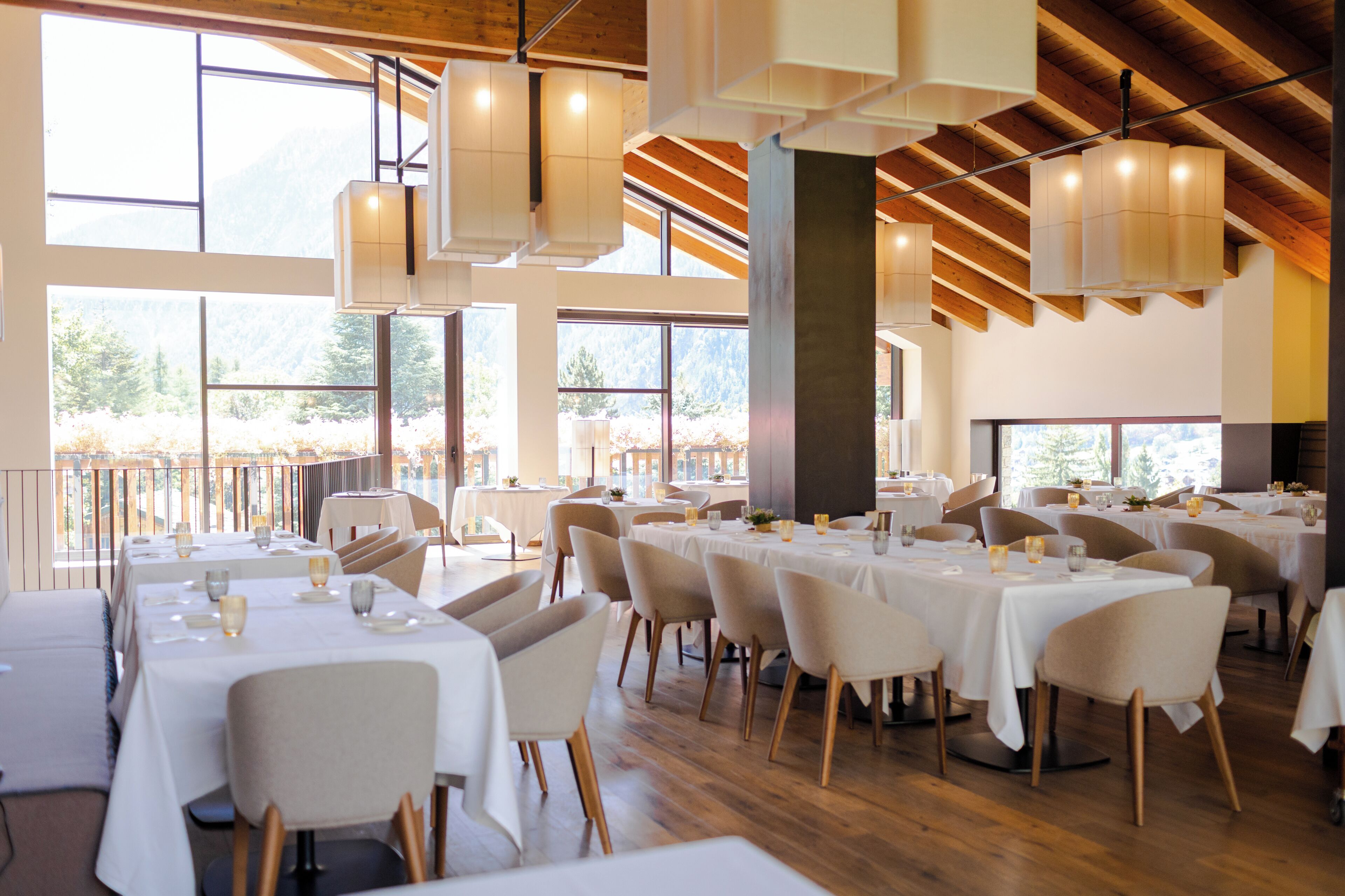 A restaurant with multiple tables and chairs, large windows, and a wooden ceiling.