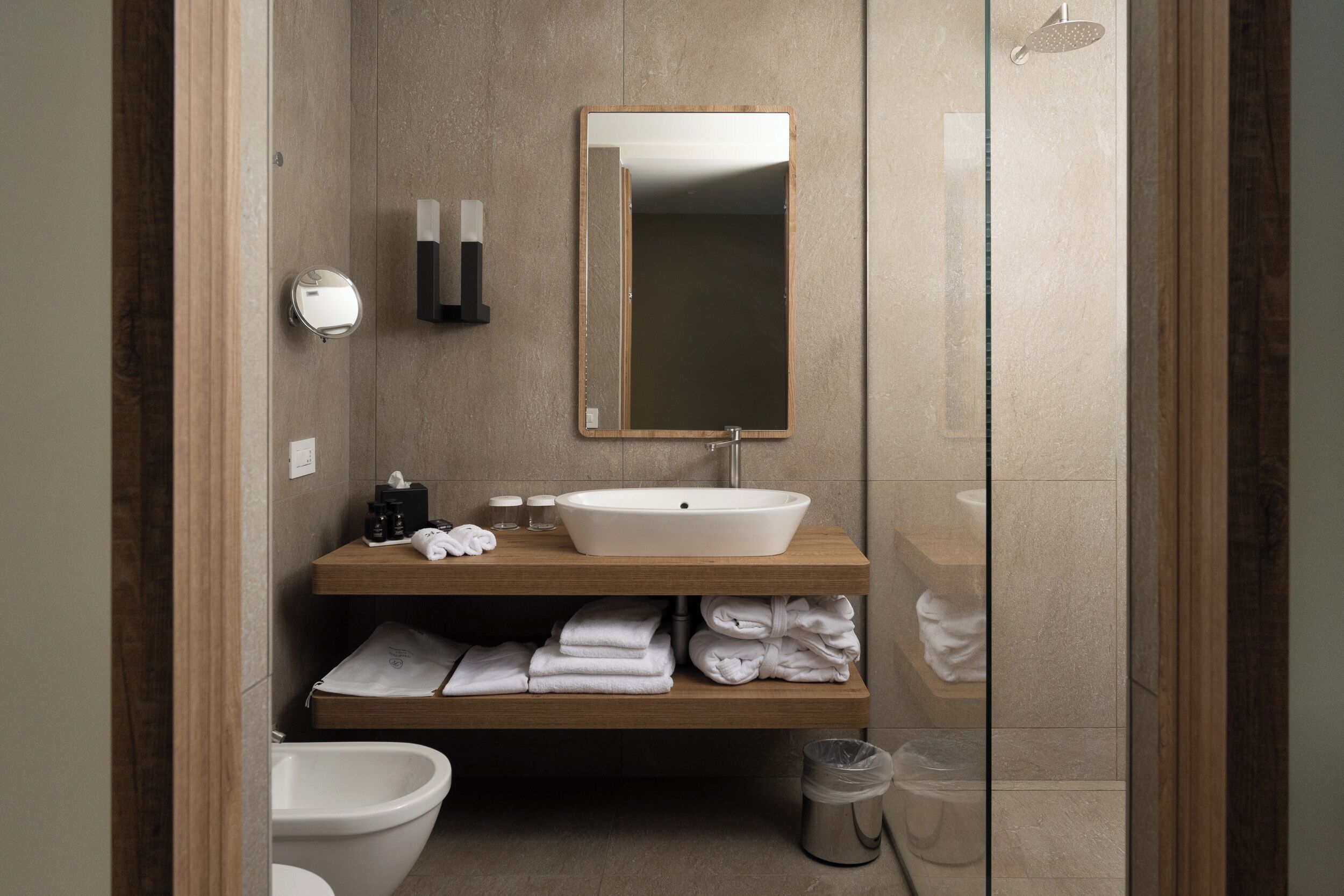 A modern bathroom with a wooden vanity, a large mirror, a white sink, and a glass shower enclosure.