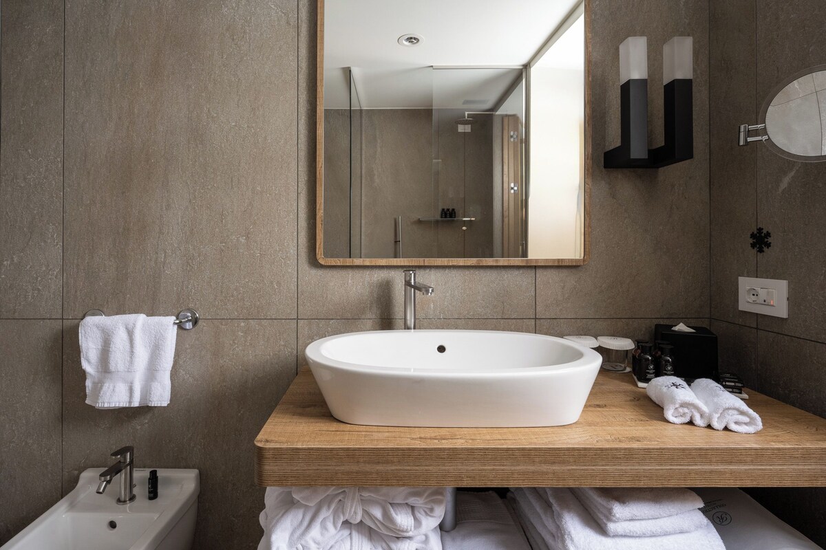 Un baño moderno con un lavamanos ovalado grande, un mueble de tocador de madera, un espejo y un perchero para toallas.