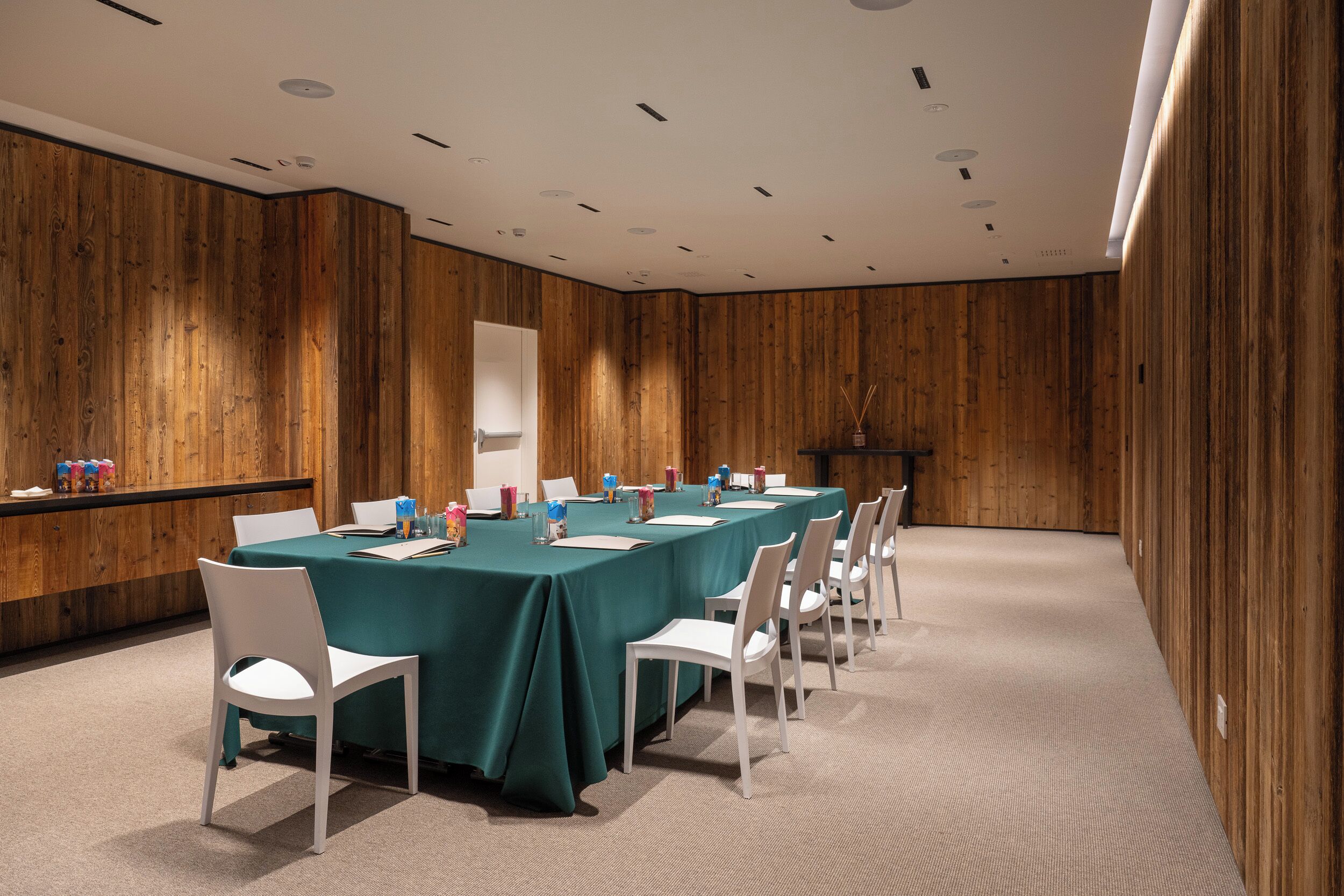 Una sala de conferencias con una larga mesa, sillas blancas y una pared de madera.