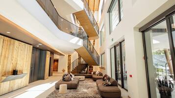 A spacious lobby with a modern design, featuring a large seating area with sofas and a coffee table, a staircase connecting multiple floors, and large windows providing natural light.