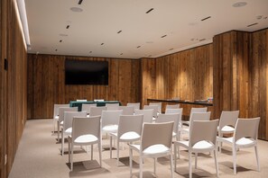 A conference room with white chairs arranged in rows, a green table, and a flat-screen TV mounted on the wall. - Grand Hotel Courmayeur Montblanc by R Collection Hotels (Courmayeur)
