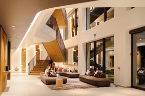 Un interior moderno con una escalera, zona de estar y ventanas amplias.