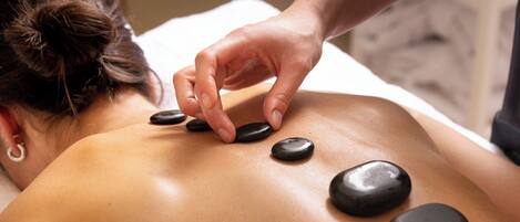 A person receiving a back massage with heated stones.