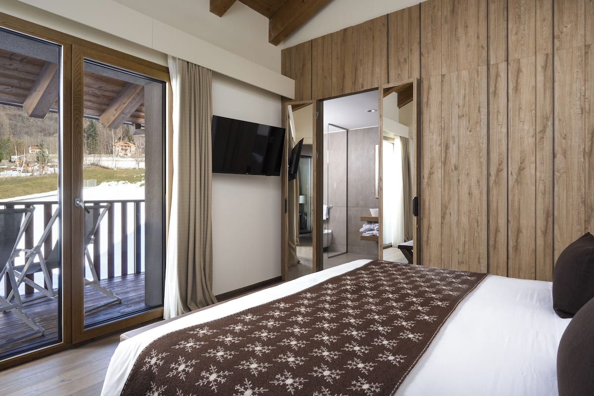 A bedroom with a large bed, a TV mounted on the wall, and a sliding glass door leading to an outdoor balcony.