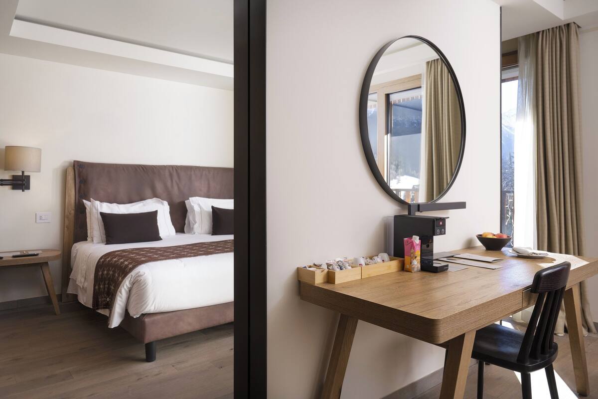 A hotel room with a bed, a desk with a mirror, a lamp, and a window with curtains.
