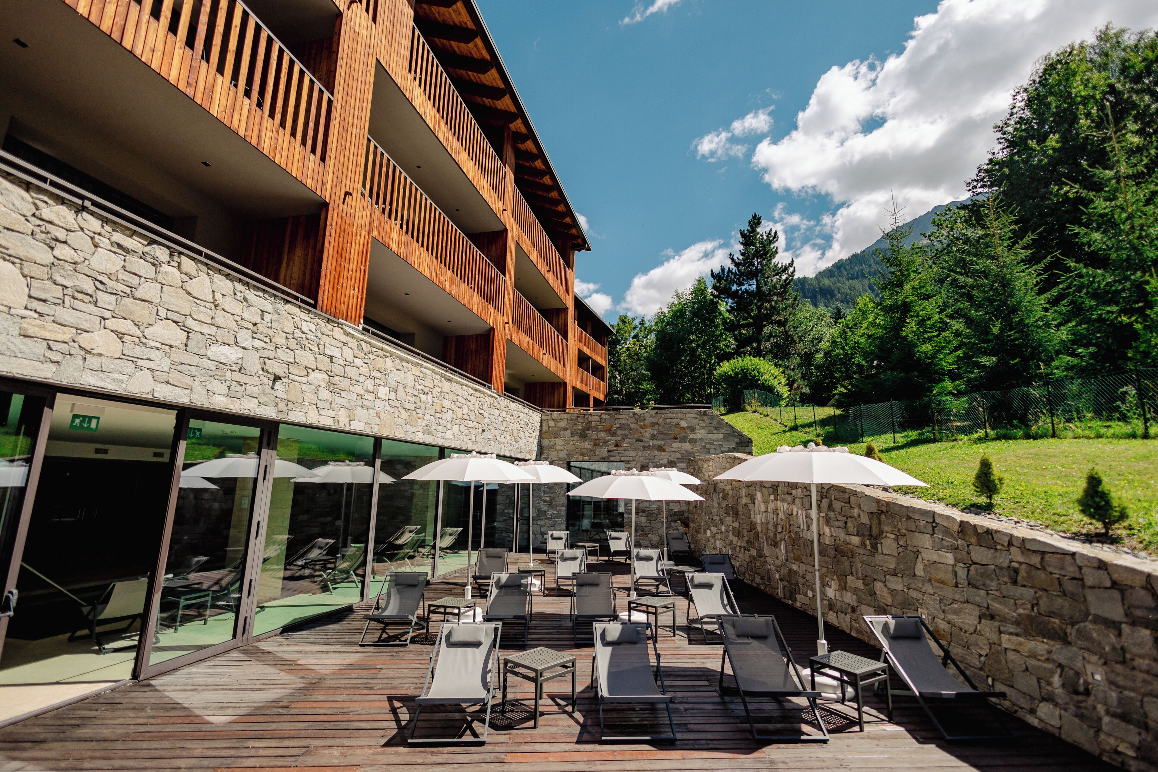 A hotel with a stone facade, wooden balconies, and outdoor seating with umbrellas.