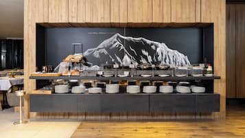 Montaje de bufé con un fondo de arte que representa una montaña, platos ordenados y una variedad de alimentos.
