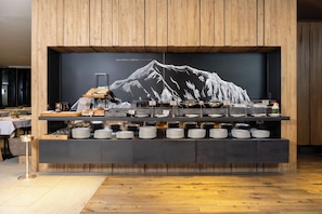 Un buffet agrémenté d’une décoration murale représentant une montagne, avec des assiettes disposées de manière soignée et une grande variété de plats proposés.