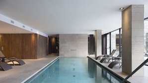 A modern indoor swimming pool with lounge chairs and a stone wall. - Grand Hotel Courmayeur Montblanc by R Collection Hotels (Courmayeur)