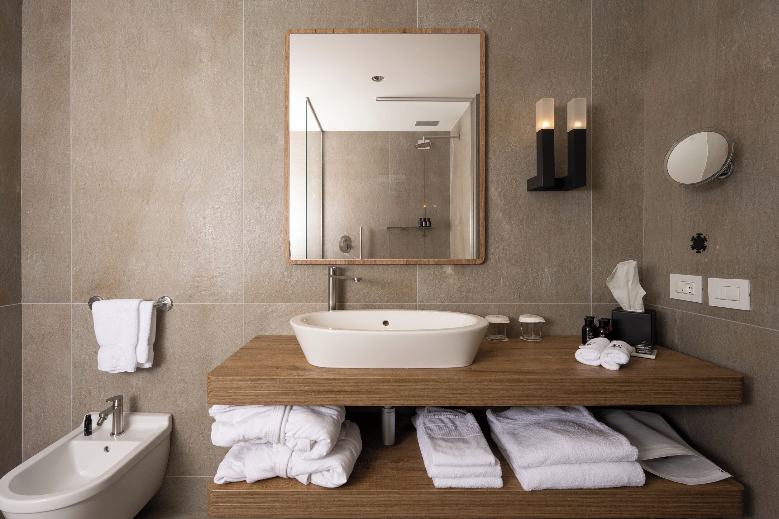 A modern bathroom with a freestanding bathtub, a sink with a mirror above it, and a vanity with towels and toiletries.