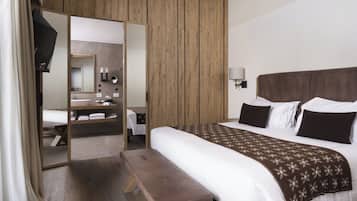 Une chambre d’hôtel moderne avec un grand lit, une armoire en bois, un banc, un miroir et une salle de bain équipée d’un lavabo et d’un miroir.
