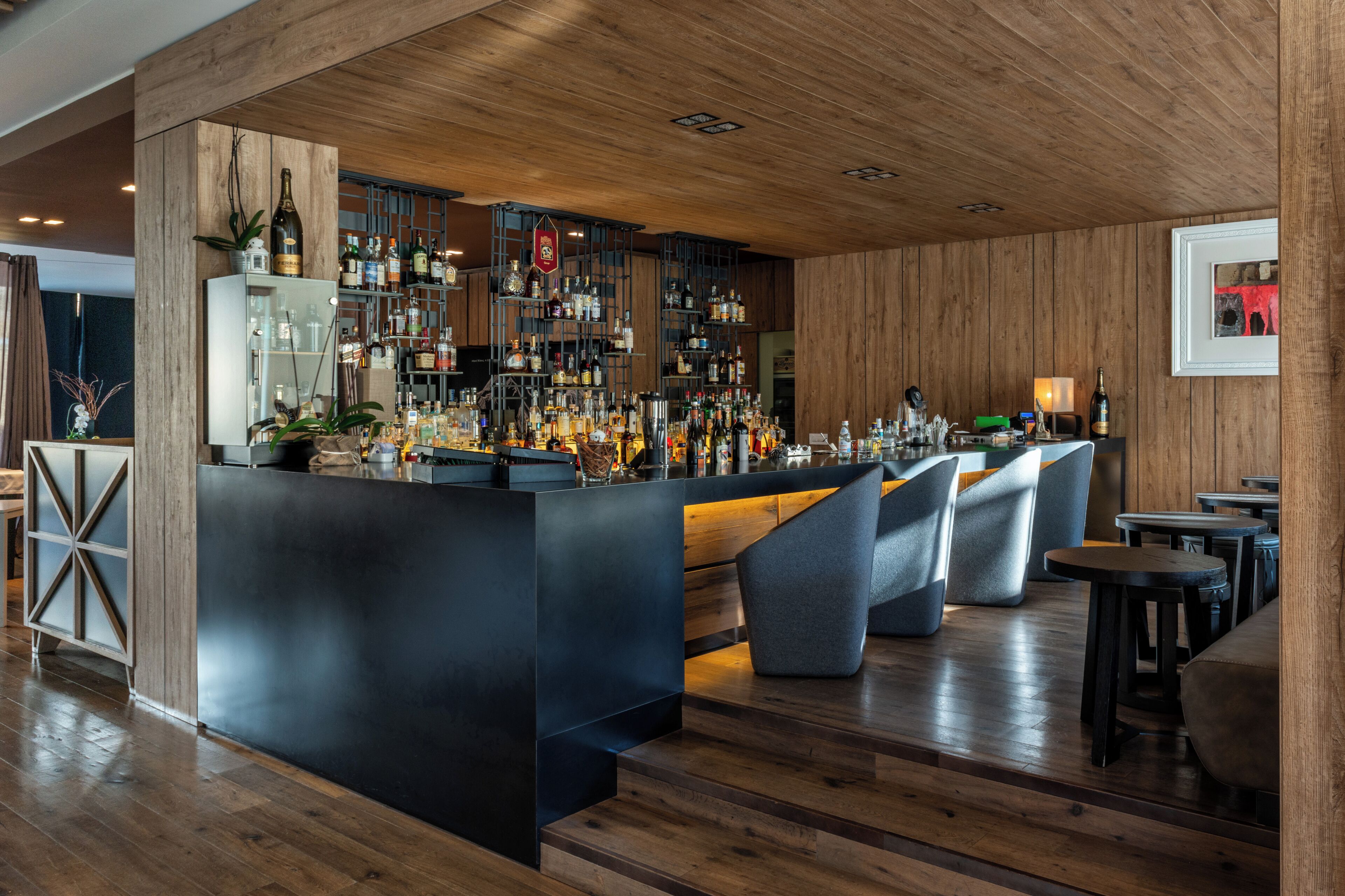 A bar area with a wooden ceiling, shelves with bottles, and seating.
