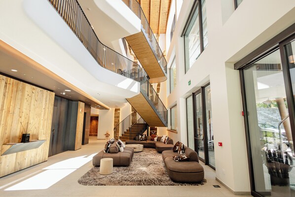 A spacious lobby with a modern design, featuring a large seating area with sofas and a coffee table, a staircase connecting multiple floors, and large windows providing natural light. - Grand Hotel Courmayeur Montblanc by R Collection Hotels (Courmayeur)