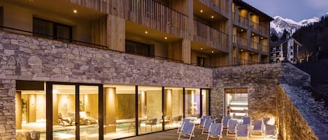 A hotel with a stone facade, multiple balconies, and a pool area with lounge chairs.