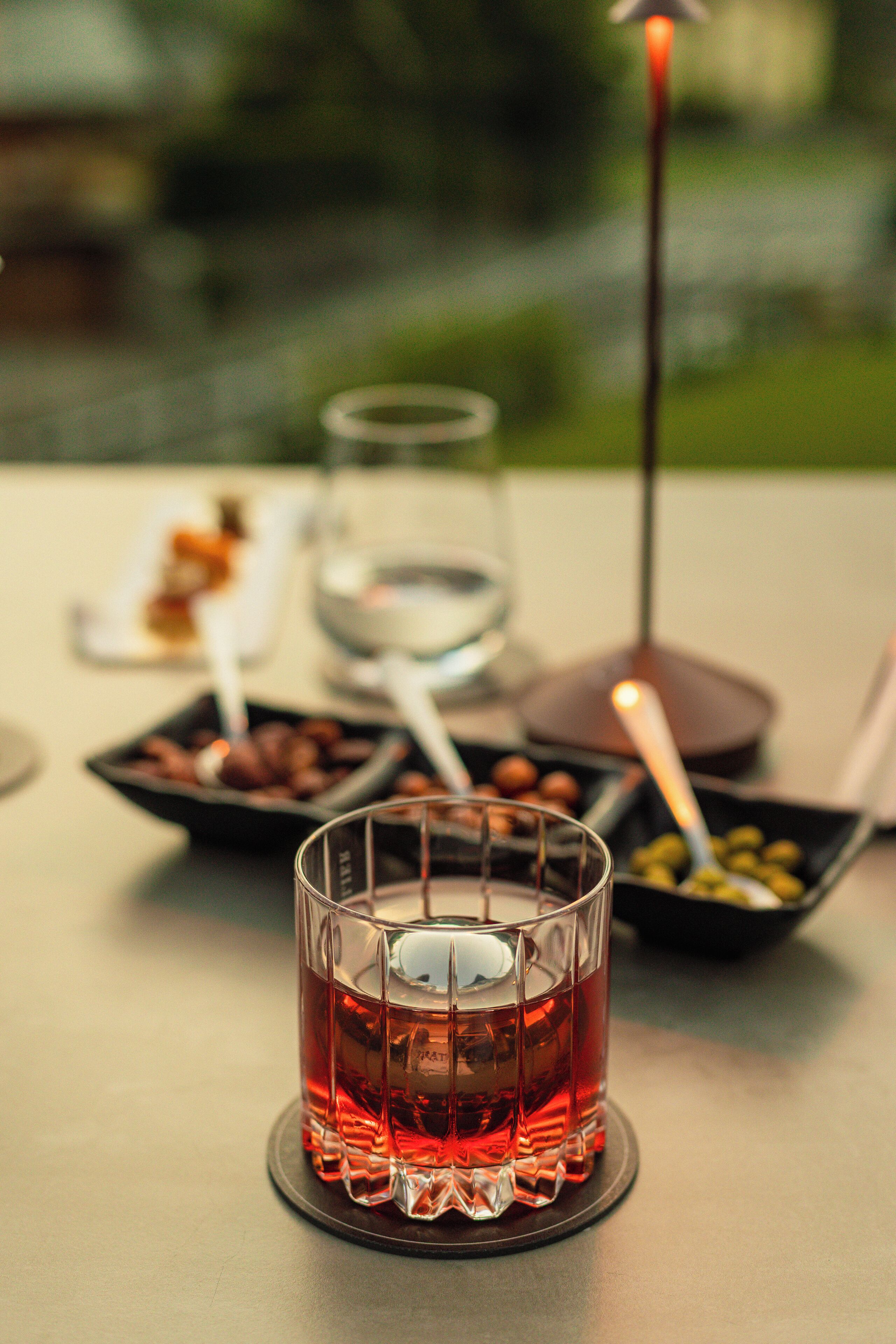Una mesa con un vaso de bebida roja, un cuenco de aceitunas y una vela.