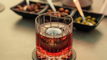 Una mesa con un vaso de bebida roja, un cuenco de aceitunas y una vela.
