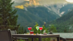 Una mesa con tres bebidas coloridas y una lámpara pequeña, frente a un paisaje de montañas.