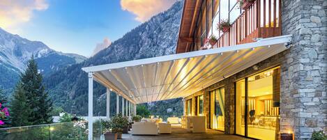 Un bâtiment moderne doté d’un patio couvert, de murs en pierre et offrant une vue sur la montagne.