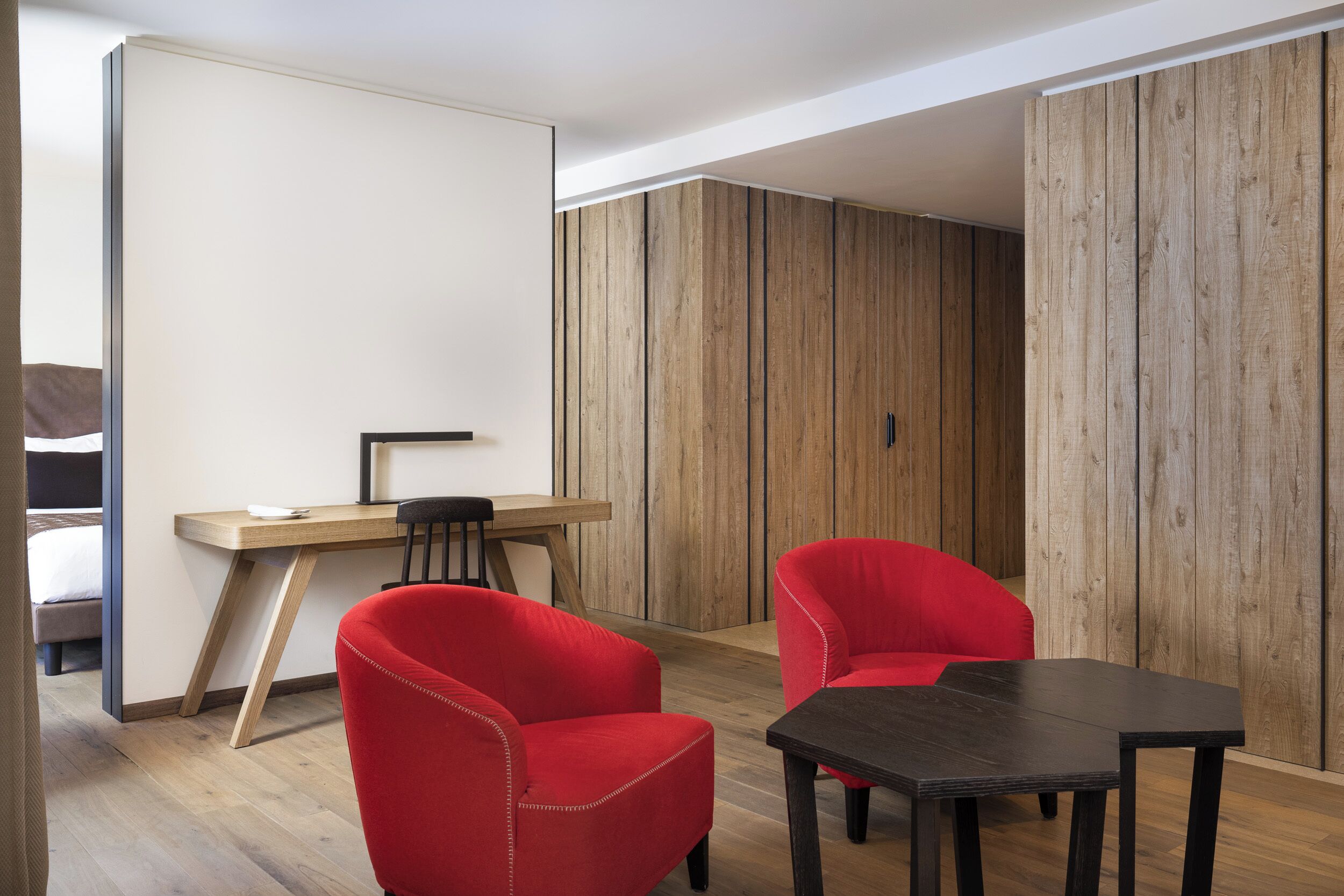 A modern room with a wooden desk, two red chairs, and a black table.