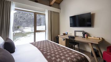 Une chambre d’hôtel avec un grand lit, un bureau avec une télévision et une vue sur un paysage enneigé.