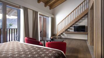 Quarto de hotel com cama, cadeiras vermelhas, uma mesinha, televisão e escada de madeira.