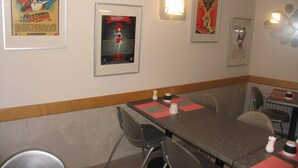 A restaurant interior with framed posters on the walls, metal chairs, and tables with red placemats. - Hôtel Saint Jean (Bourges)