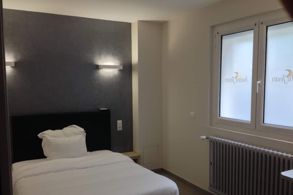 Une chambre d’hôtel avec un lit, une table de chevet, une fenêtre donnant sur un paysage agréable et un luminaire fixé au mur.