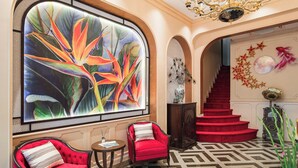 A grand lobby with a large abstract painting, a chandelier, red upholstered chairs, a staircase, and a patterned floor. - Hanoi Little Town Hotel (Hanoi)