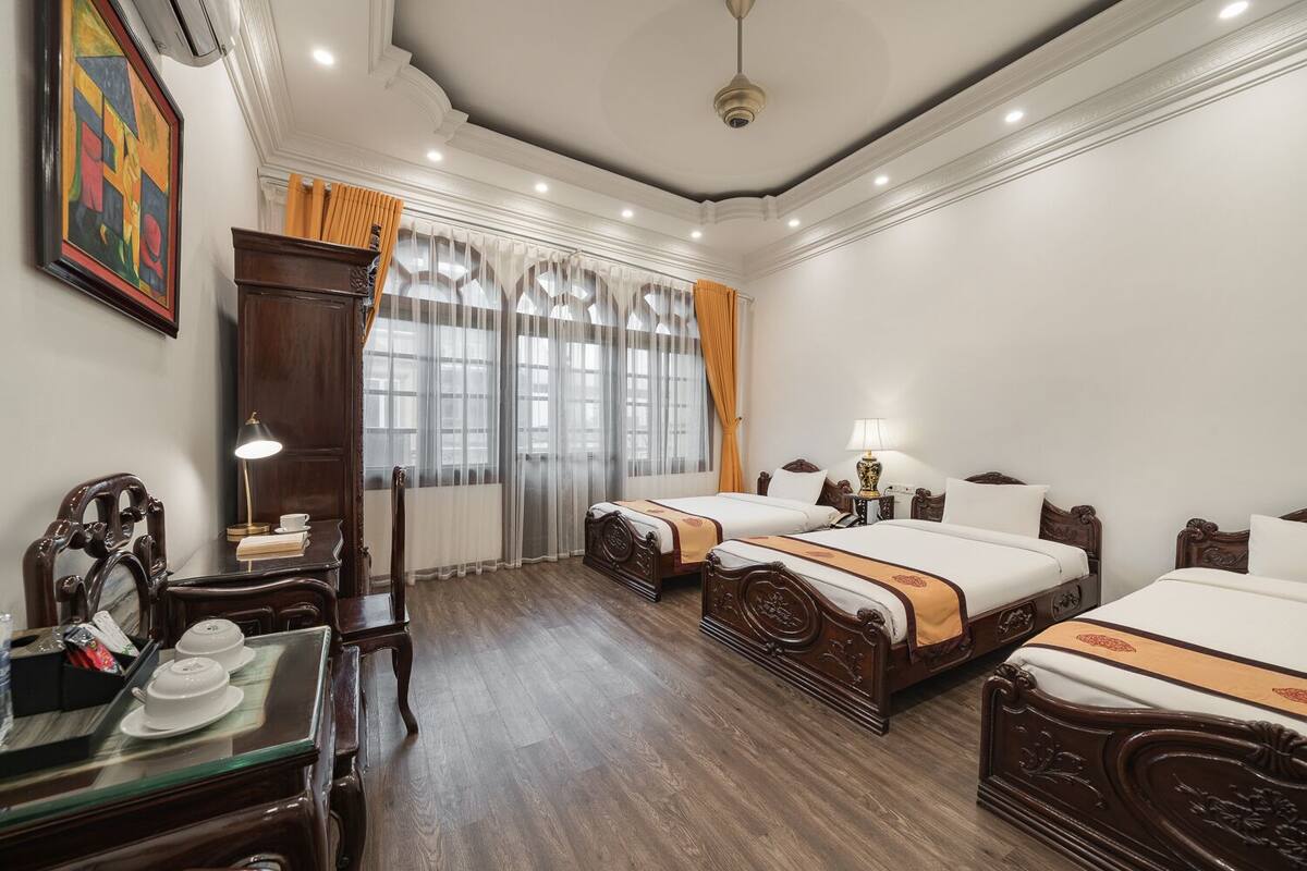 A hotel room with two wooden beds, a wooden desk with a chair, a large mirror, and a painting on the wall.
