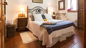 A neatly arranged bedroom with a bed, bedside tables, a dresser, a wicker basket, and a window with flowers. - Finca El Picacho (San Cristóbal de La Laguna)
