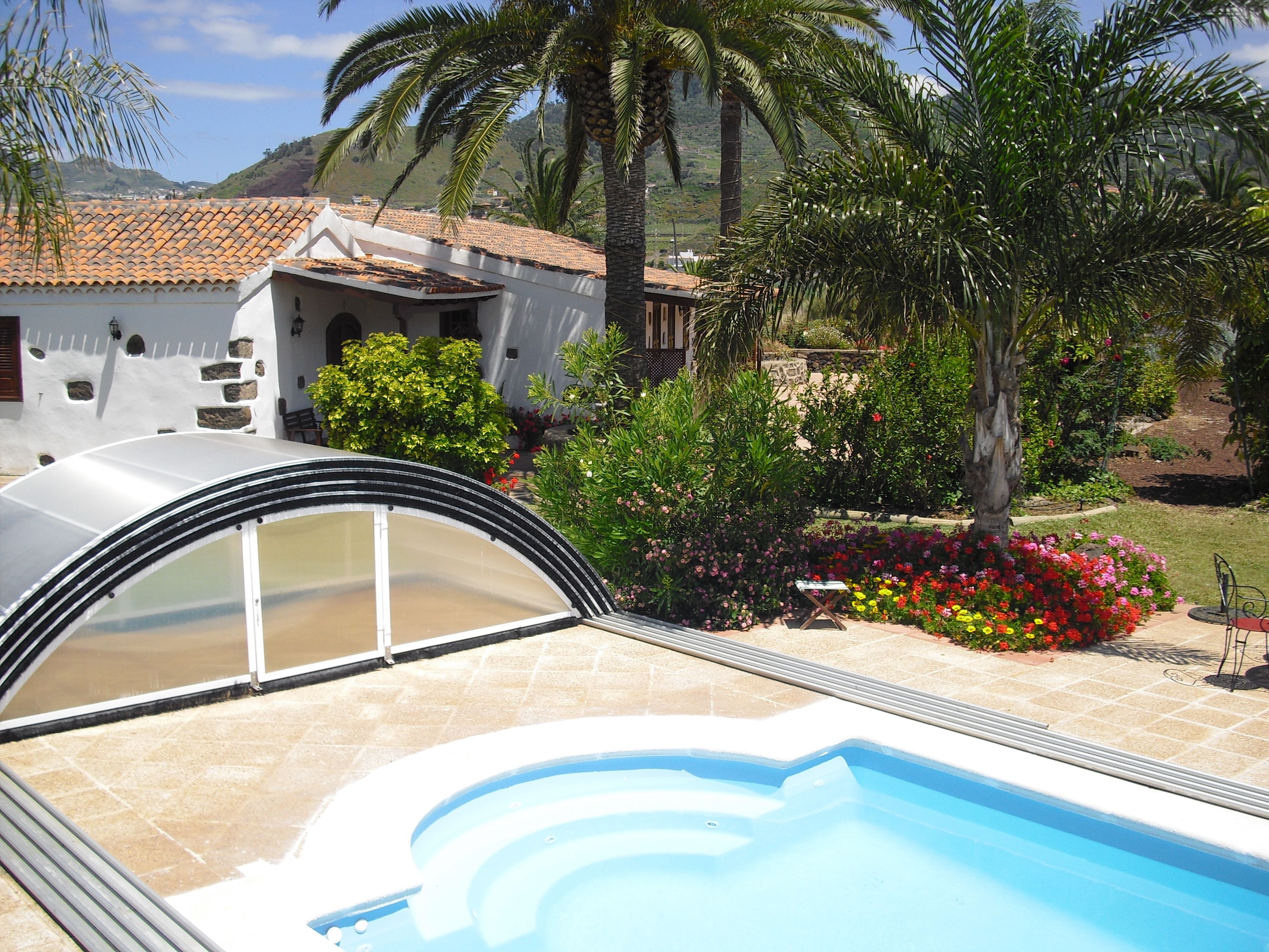 Piscina con cerramiento de vidrio curvo, rodeada por un jardín con diversas plantas y flores.