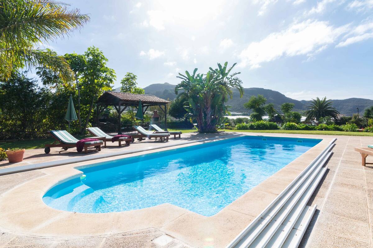 Una piscina con sillas de descanso y un pabellón, rodeada de follaje y montañas.