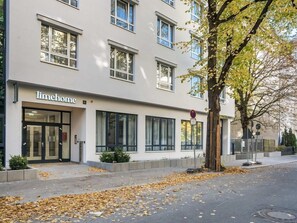 A building with a sign reading 'limehome' on the ground floor, large windows, and a tree with autumn leaves. - Hotel Alt-Tempelhof (Berlin)