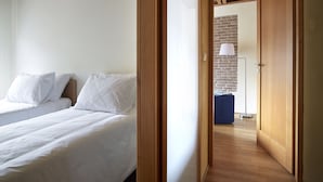 Ein Schlafzimmer mit zwei Betten, einer Holzbalkendecke, einer Ziegelwand und einem blauen Hocker.