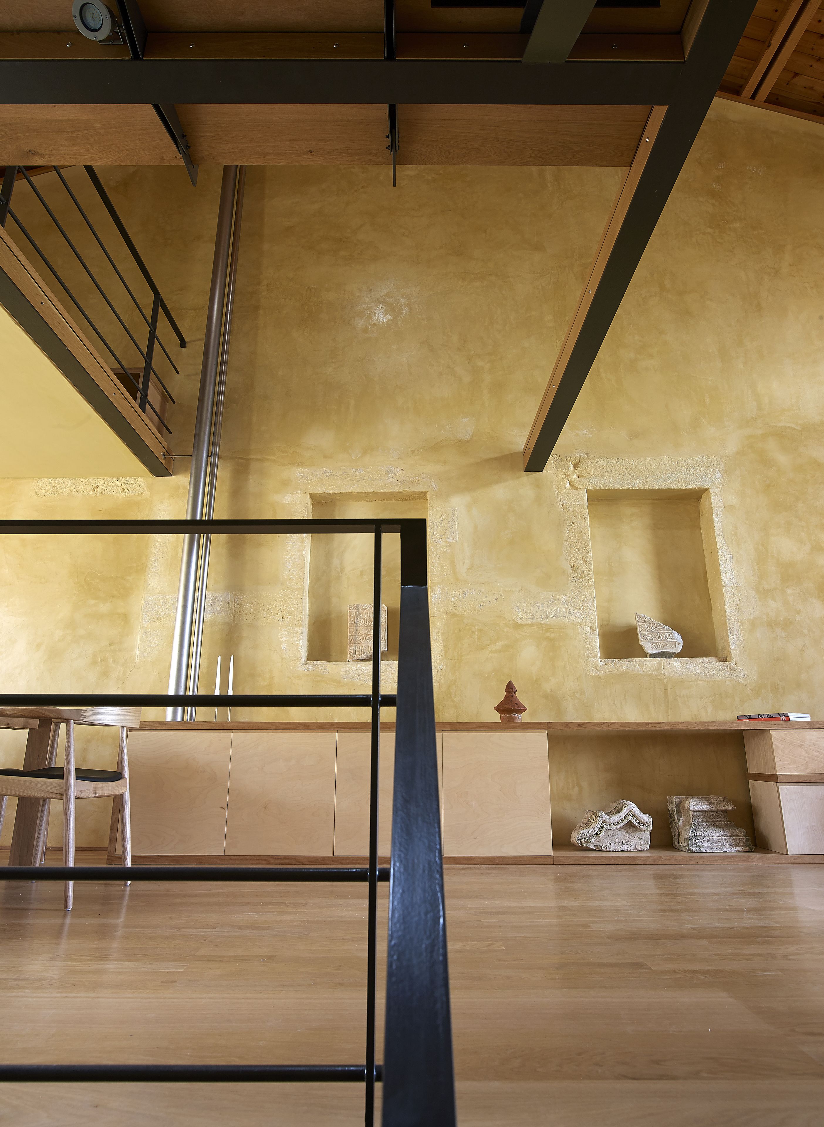 Una habitación con piso de madera, baranda de metal negro y ventana con vista al cielo.