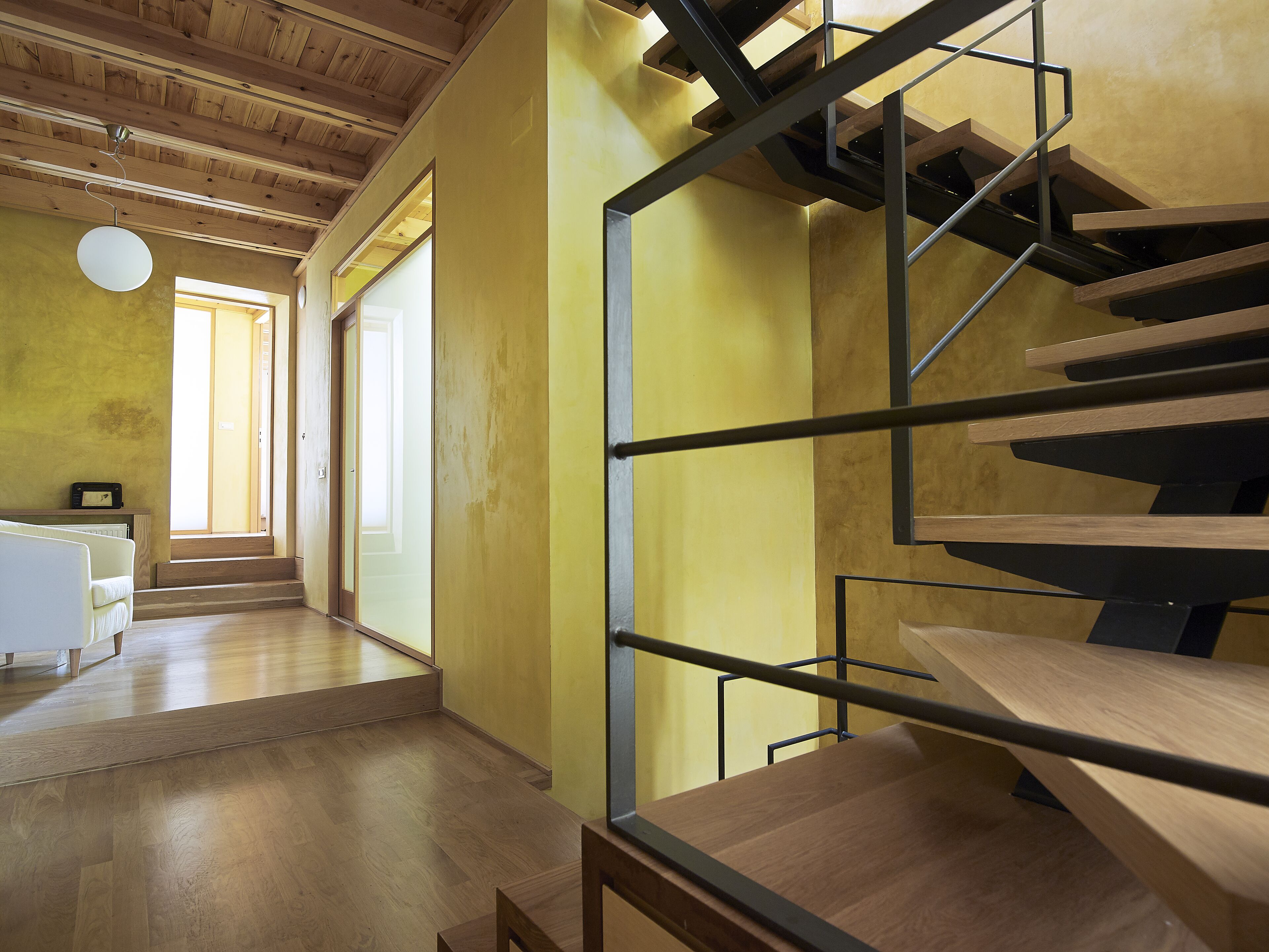 A modern interior with a wooden staircase, a white sofa, and a wooden floor.