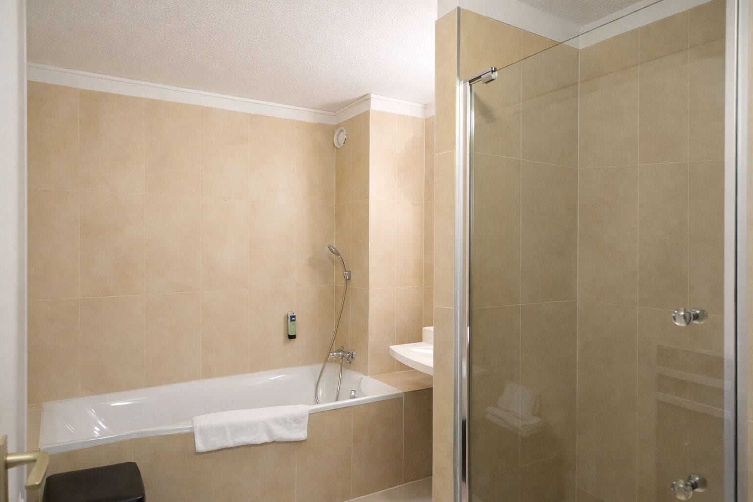 A bathroom with a bathtub, a glass shower enclosure, and beige tiled walls.