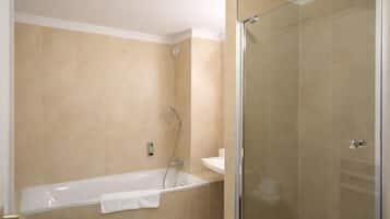 A bathroom with a bathtub, a glass shower enclosure, and beige tiled walls.