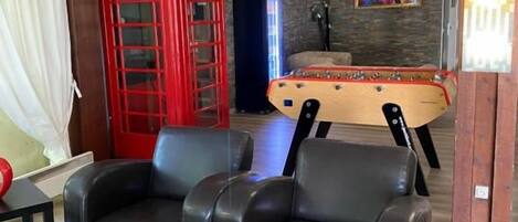 A room with a red telephone booth, two black leather sofas, a pool table, and a cowhide ottoman.