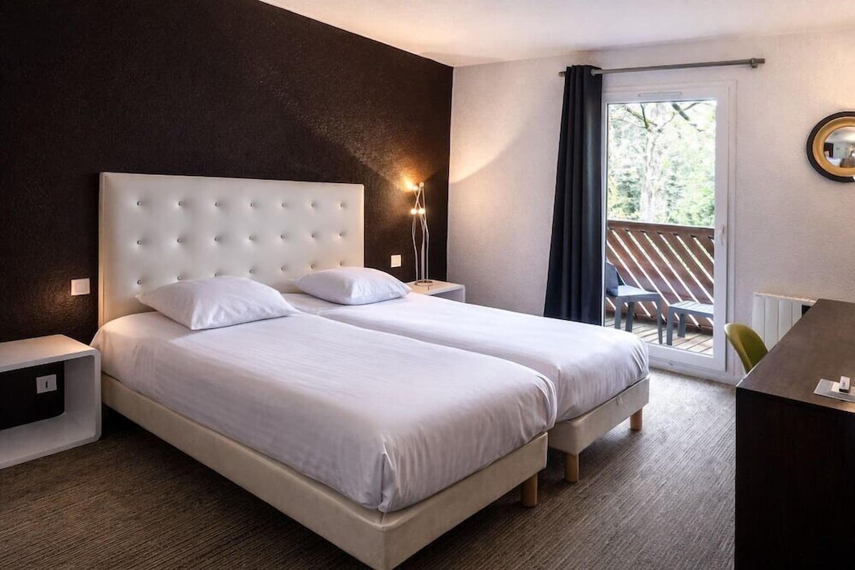 A double bed with a tufted headboard, a bedside table, a lamp, a chair, and a view of the outdoors through a sliding door.