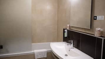 A modern bathroom with a white sink, dark wall paneling, a mirror, and a towel on the floor.