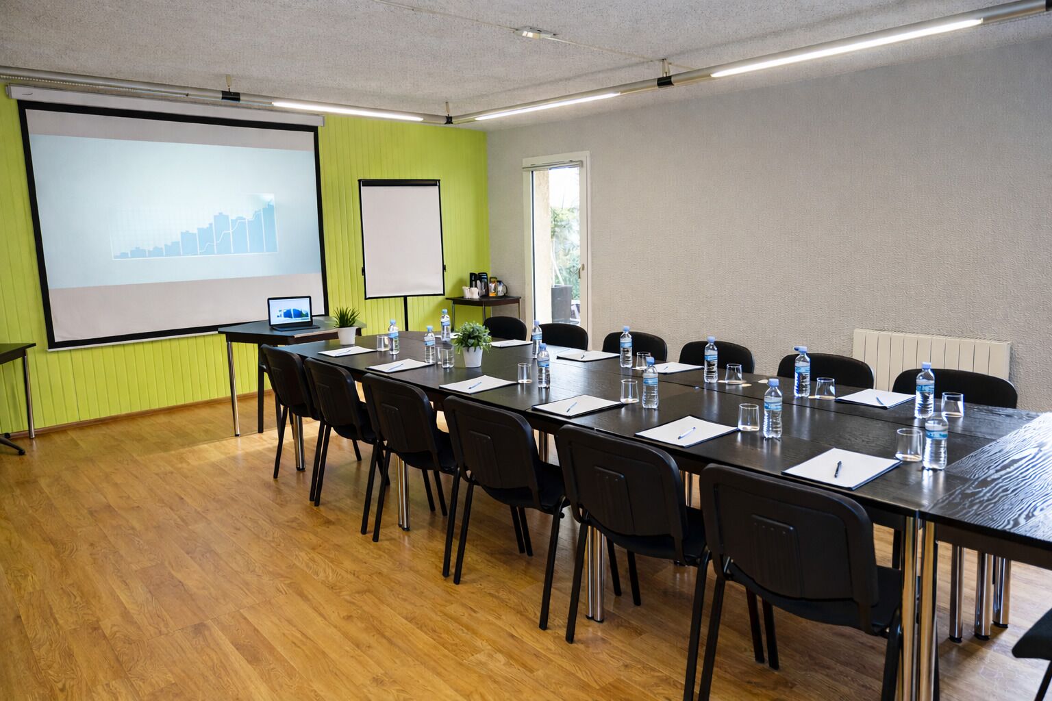 A conference room with a long table, chairs, a projector screen, and a whiteboard.