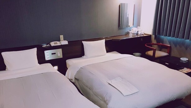 Ein Hotelzimmer mit zwei Betten, einem Schreibtisch, einem Stuhl und einem Spiegel.