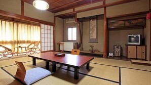 A traditional Japanese room with tatami flooring, a low table, a cushioned bench, a television, and a sliding door. - Azumaya (Tanabe)