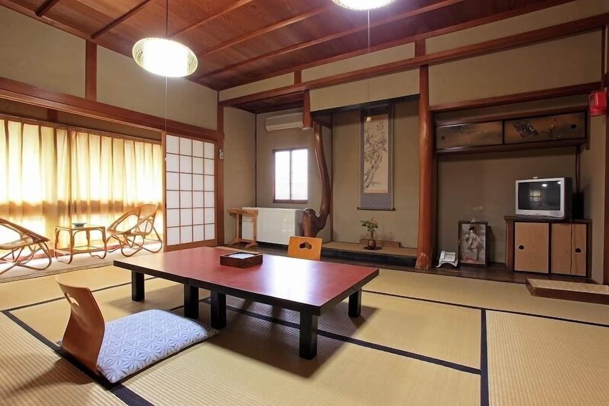 A traditional Japanese room with tatami flooring, a low table, a cushioned bench, a television, and a sliding door.