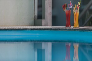 Two cocktails with fruit garnishes by a poolside.