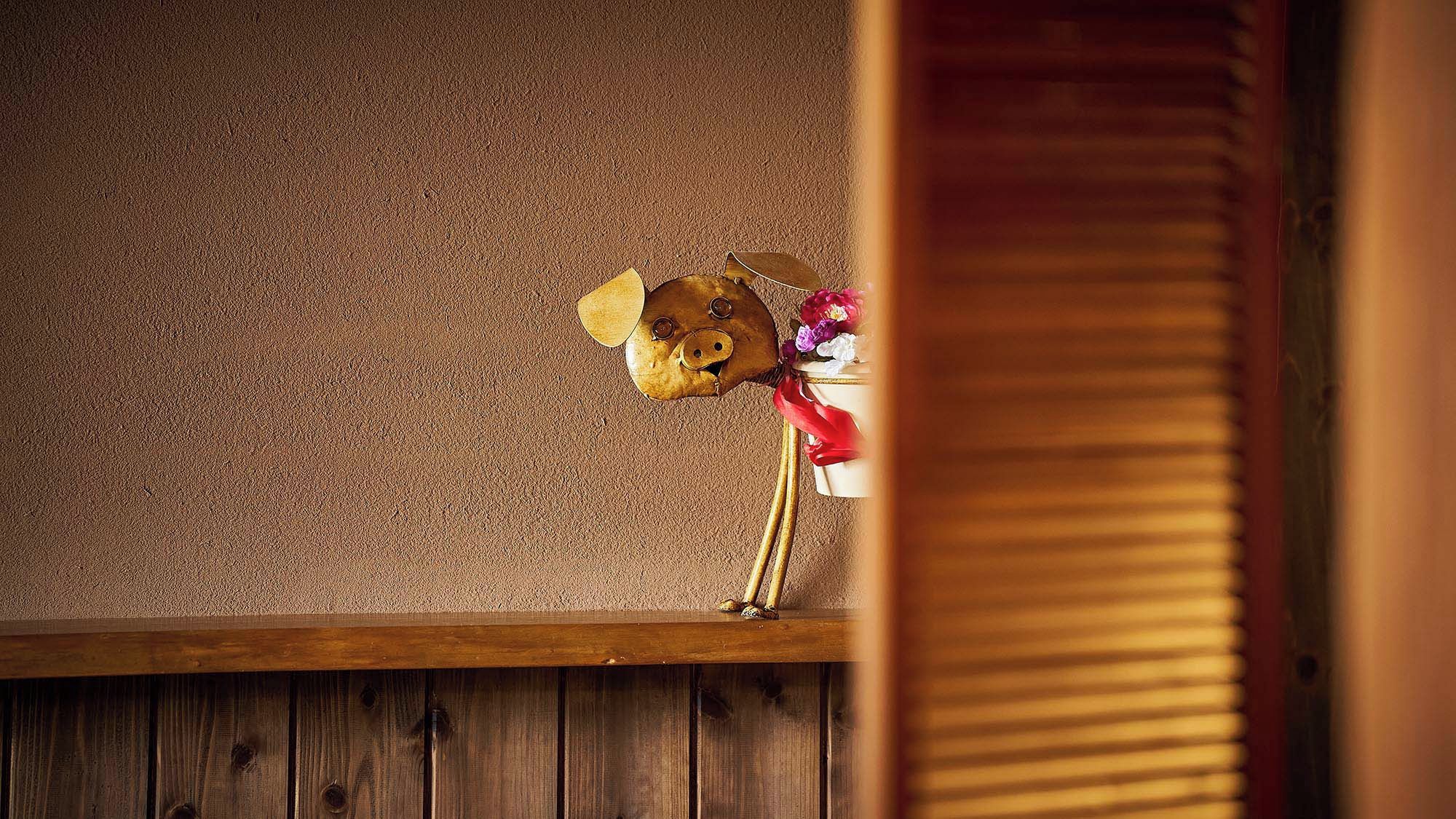 Un cerdito hucha con un ramo de flores sobre un estante de madera frente a una pared con textura.