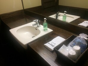 Un baño de hotel con un lavamanos blanco, un espejo y artículos de aseo en una cesta.